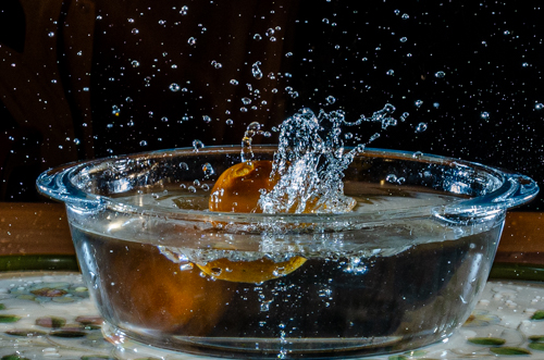 Tangerine splashing into bowl of water